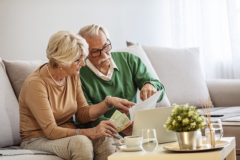 a couple in their 70s sits on a couch together, reviewing paperwork