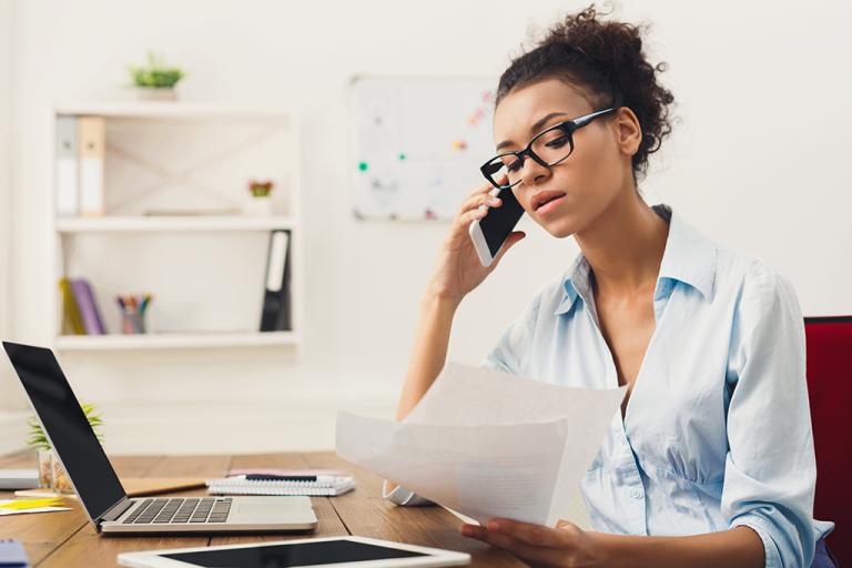 A woman with a laptop and paperwork making a phone call