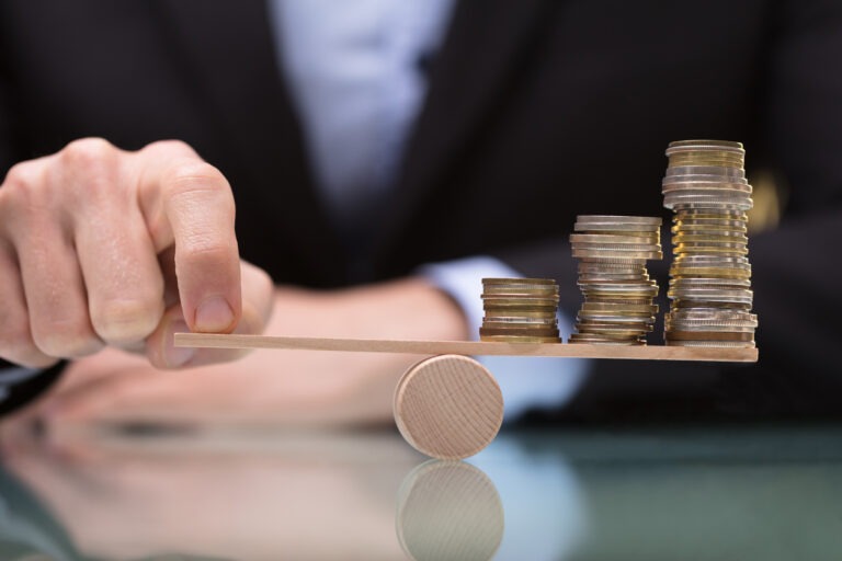 Closeup of man balancing coins on a wooden balance beam