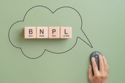 BNPL, buy now pay later, on wooden cube block inside speech bubble and black wireless mouse on green background