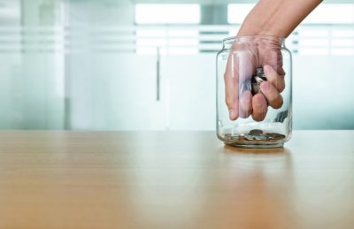 Hand grabbing coins from glass jar.