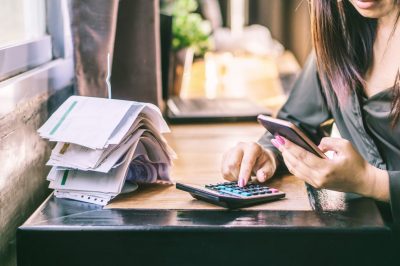 woman hand calculating her monthly expenses and debt during tax season with financial bills on desk