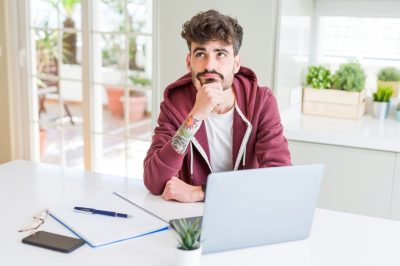 Young man at computer in kitchen with questioning facial expression