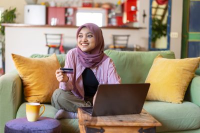 Woman on couch holding credit card near laptop