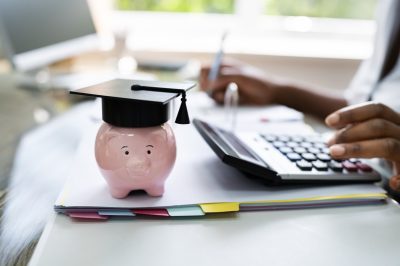 Woman at desk with calculator. Piggy bank with graduation cap on desk.
