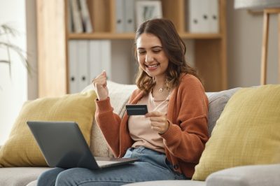Excited, woman and laptop with credit card, banking and online shopping with fintech, transaction and happiness in a lounge. Person, home and girl on a couch, pc and celebration with payment or bonus