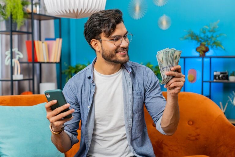 Man on couch holding cash in one hand and phone in other
