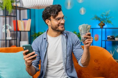 Man on couch holding cash in one hand and phone in other