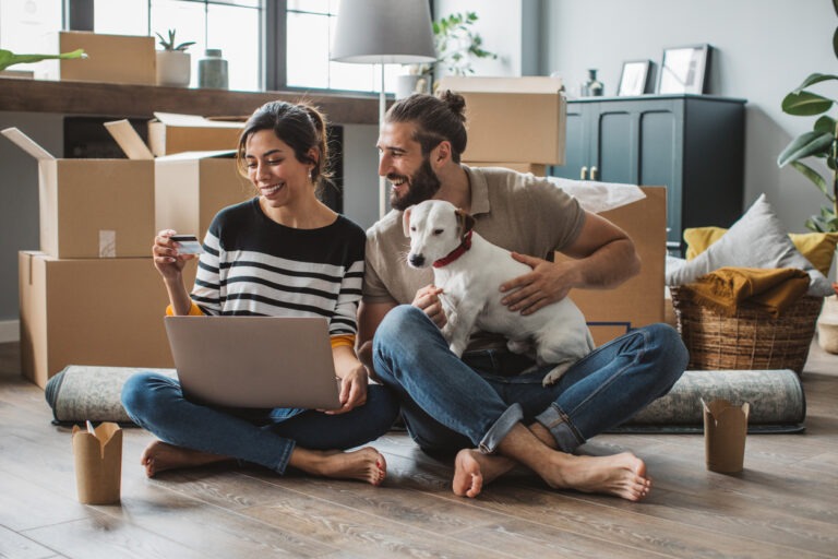 Young couple moving in new house. They are happy and using laptop to buy stuff they need.