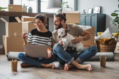 Young couple moving in new house. They are happy and using laptop to buy stuff they need.