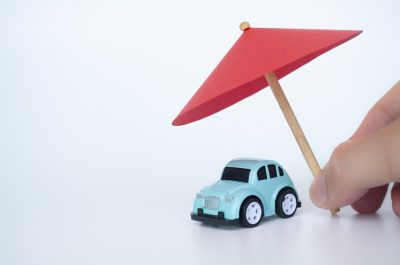 Toy car covered with toy umbrella representing car insurance concept.