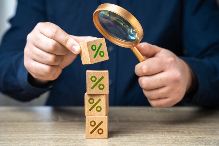 Man with magnifying glass looking at wooden cubes with "%" signs on them