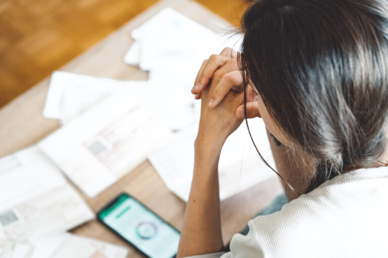 Woman looking at phone applying for loan with mess of documents on desk
