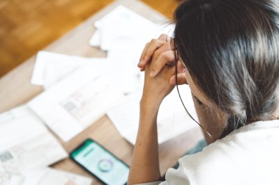 Woman looking at phone applying for loan with mess of documents on desk