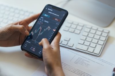 Close-up Shot of an Anonymous Woman Holding a Smartphone with a Stock Market Graph on Screen