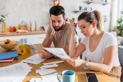 Worried young couple checking the finances on a digital tablet in the living room.