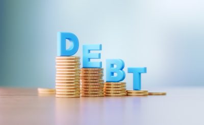 Blue capital letters sitting on coins stacks write debt before defocused background.