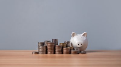 Piggy bank and coins lined up on a wooden floor with a white background. Concepts of finance, savings and investment.