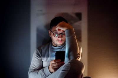 Man in dark room looking at phone, stressed.